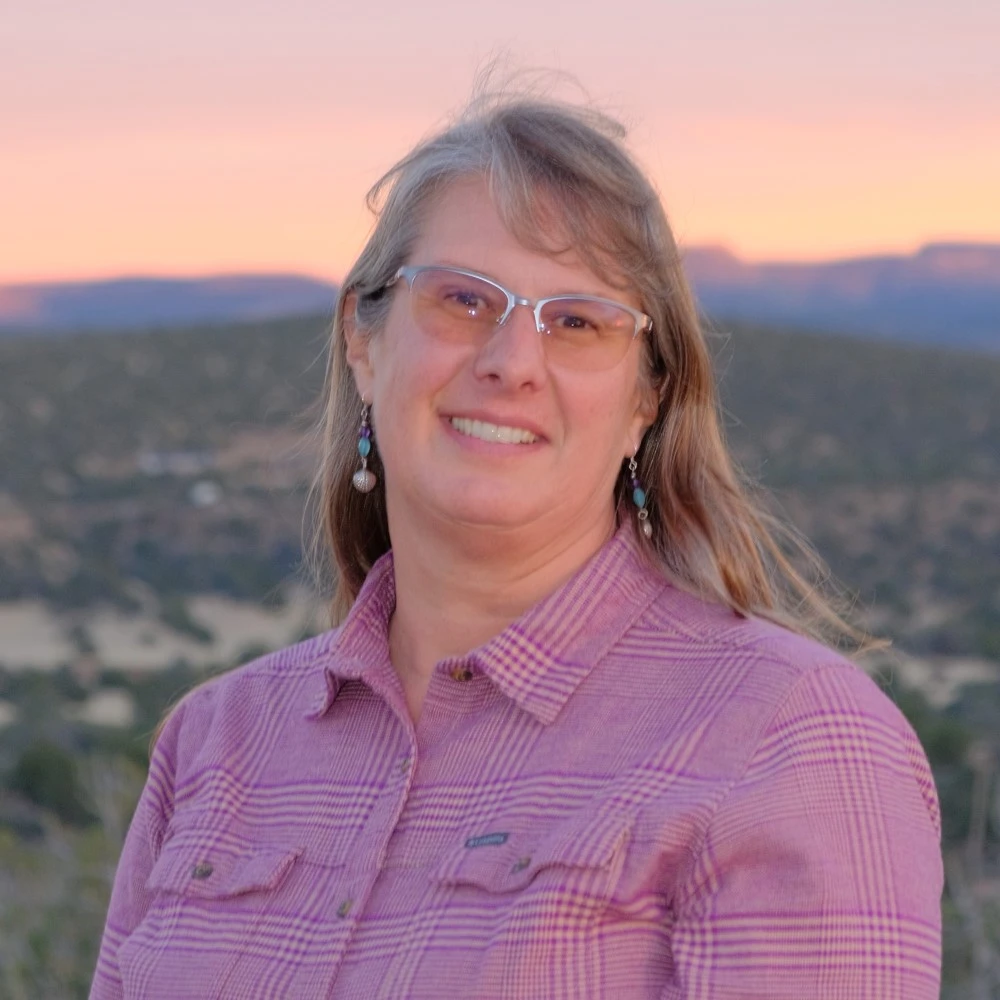 A headshot of the Realtor Cheryl Robertson, smiling at the camera. She is dressed semi-formally with mountains in the backdrop.